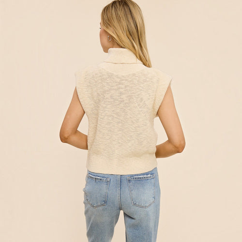 Back view of a Minimistcloset cream 100% cotton structured knit turtleneck top with cap sleeves on a model.
